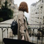 Woman in trench coat walking through a Parisian street with an umbrella, showcasing city life and travel.